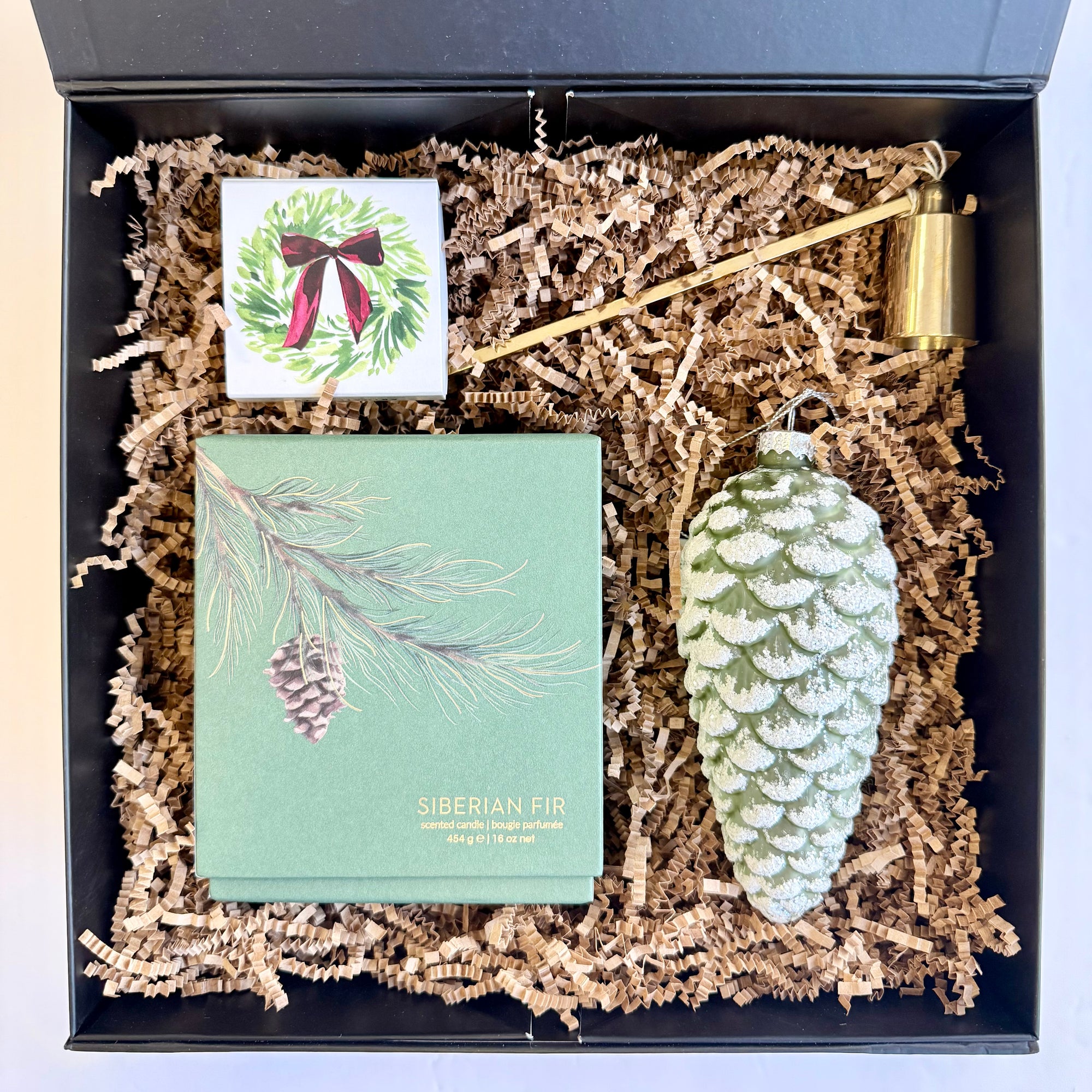 Decorative gift set with a pine cone ornament, card, and box in a black box.