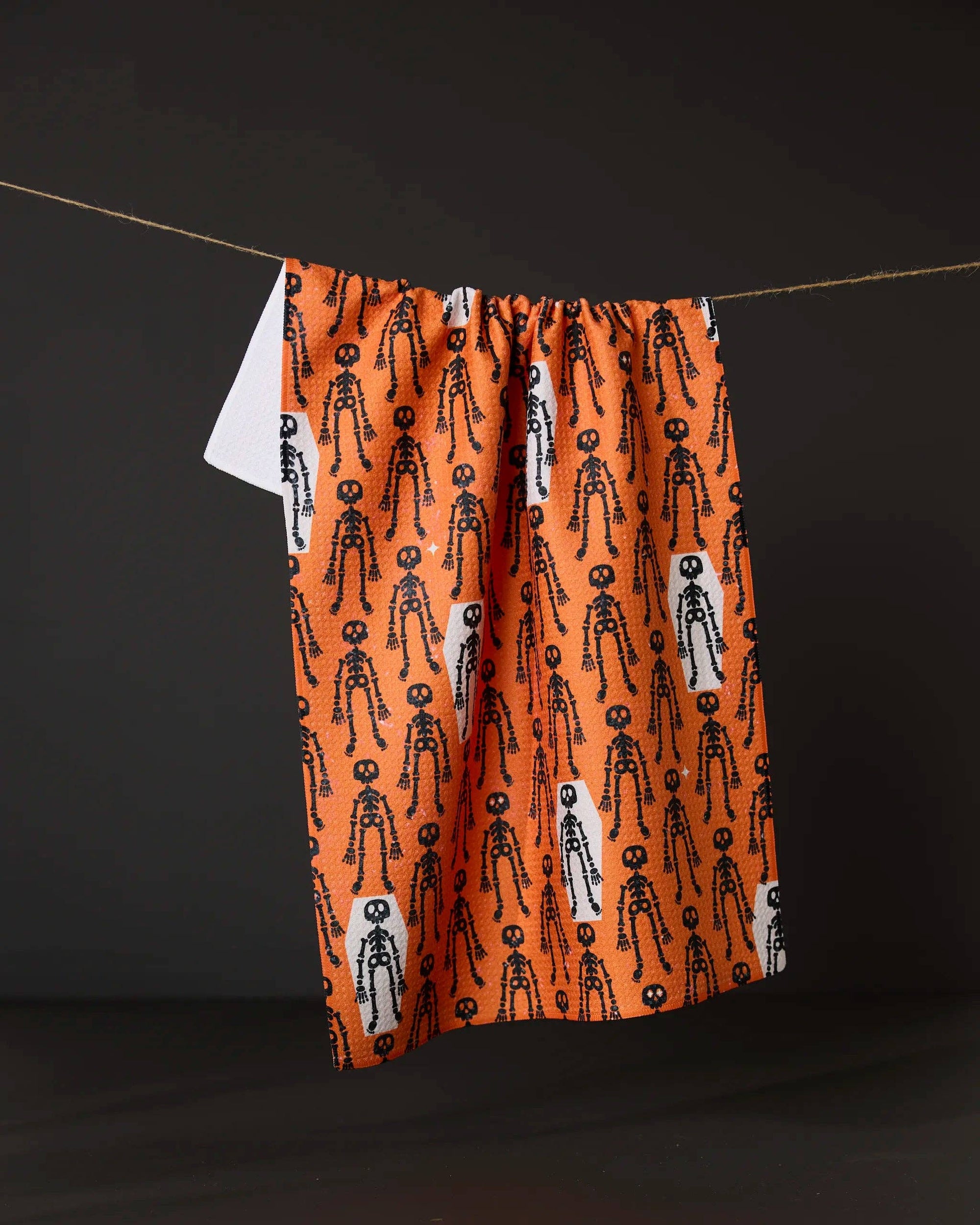 Resting Skeletons Orange Tea Towel made from recycled materials hanging in kitchen