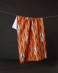 Resting Skeletons Orange Tea Towel made from recycled materials hanging in kitchen